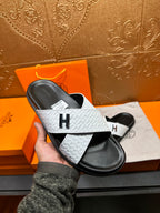Hand holding a white textured slide sandal with black footbed and H on strap