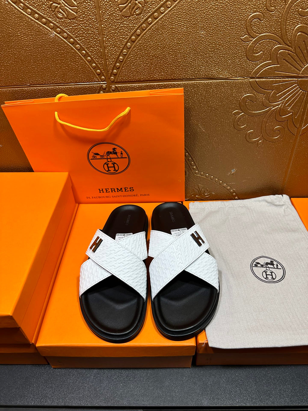 White slide sandals with black footbed and cross strap featuring a single H emblem