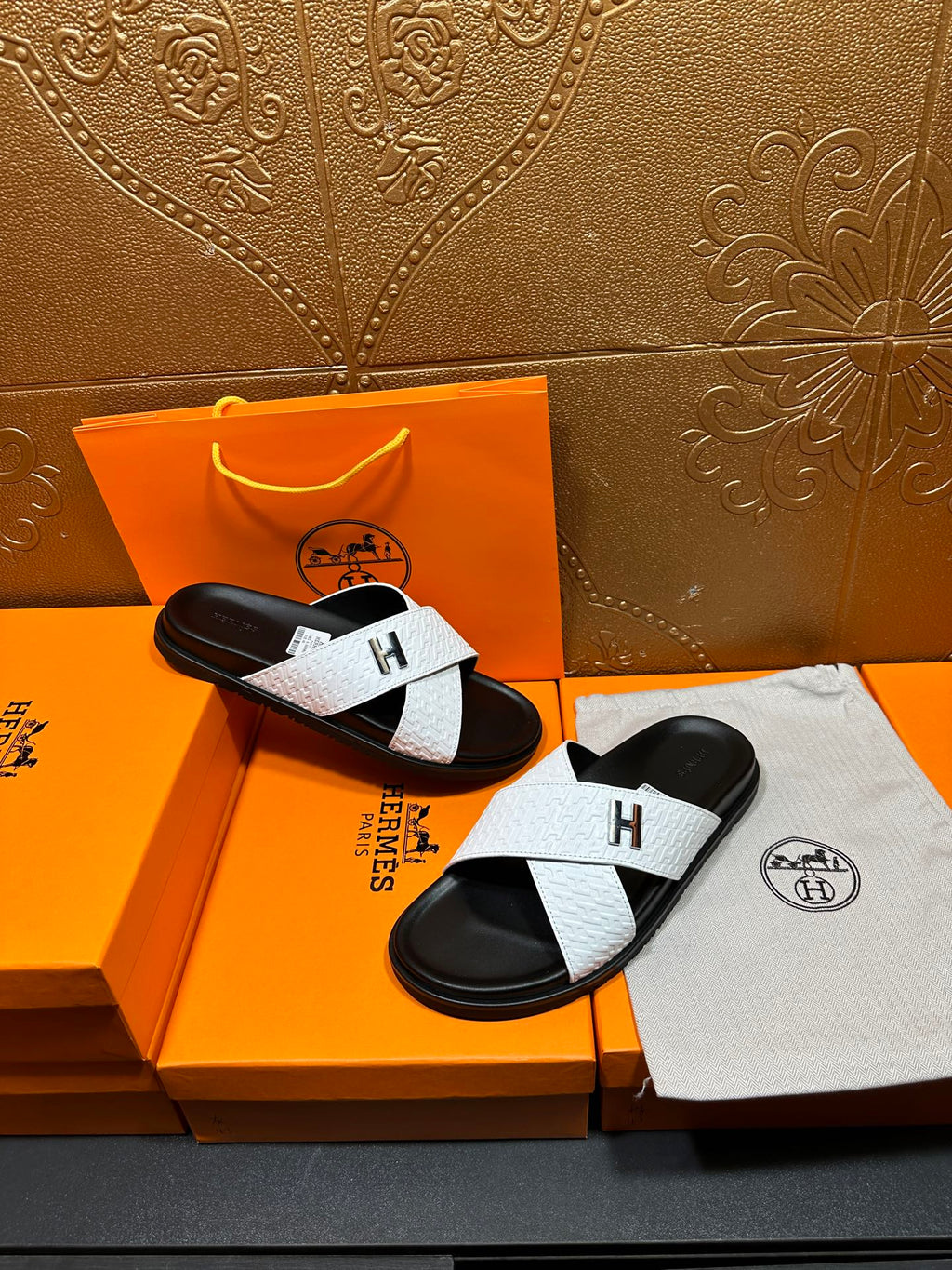 White and black H logo slide sandals on a box, showing both left and right shoes