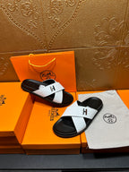 White and black H logo slide sandals on a box, showing both left and right shoes