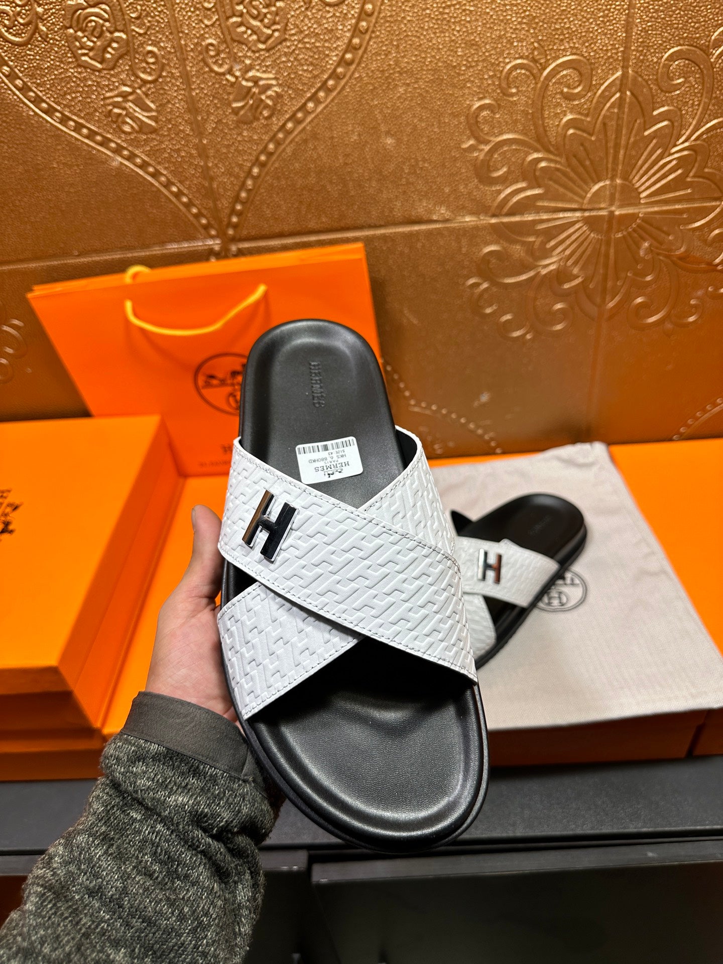 Hand-held white slide sandal with black sole and H emblem on the cross strap