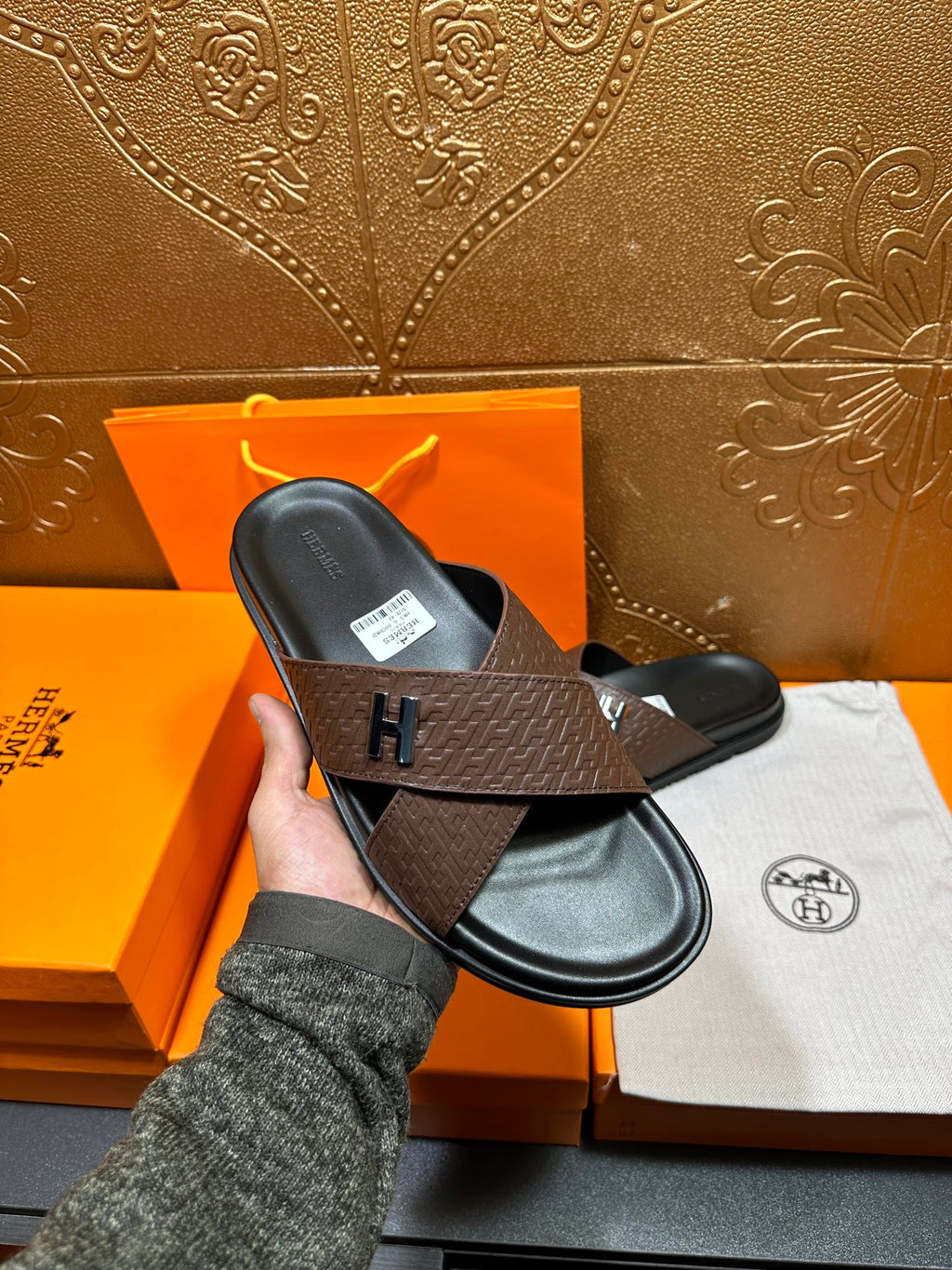 Brown textured leather slide sandals held in hand, black footbed, H buckle