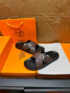 Pair of brown slide sandals with black footbed and H logo strap on a tray