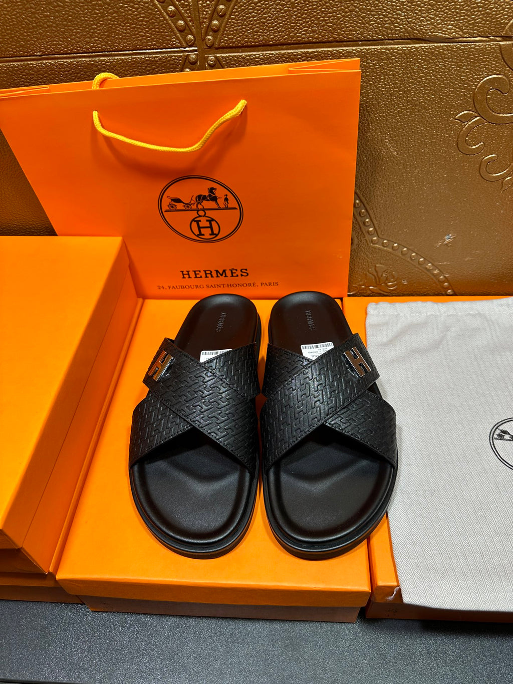 Black slide sandals with textured straps and H buckle, flat sole