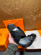 Single black textured slide sandal with H buckle, held in hand