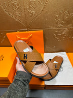 Hermes slide sandal held in hand, tan textured strap with H buckle, open toe