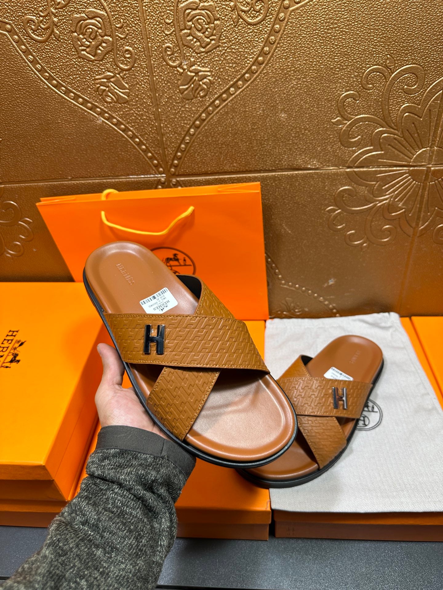 Hermes slide sandal held in hand, tan textured strap with H buckle, open toe