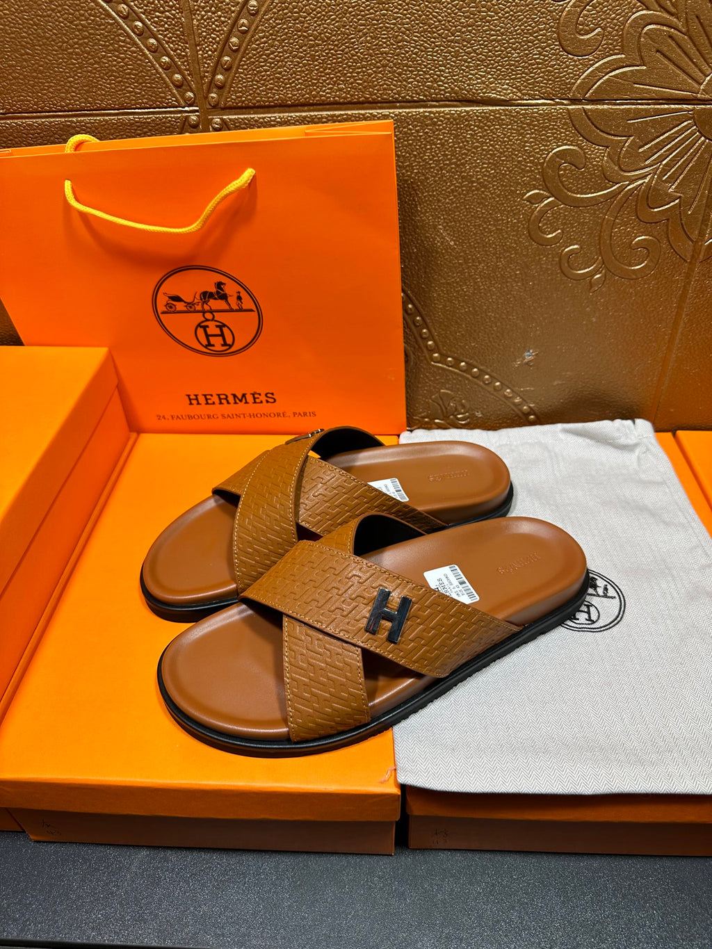 Hermes slide sandals with tan textured straps and H buckle, pair side-by-side