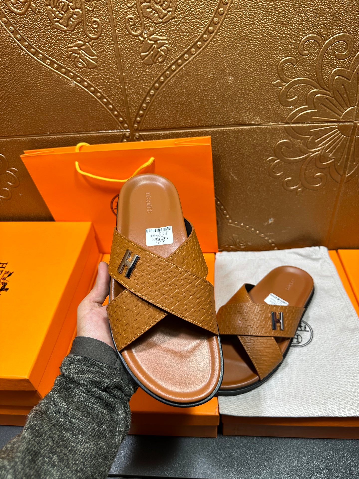 Hermes slide sandal held in hand, tan textured H-strap slide, open-toe
