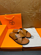 Hermes slide sandals with tan textured cross straps and H buckle, one sandal angled