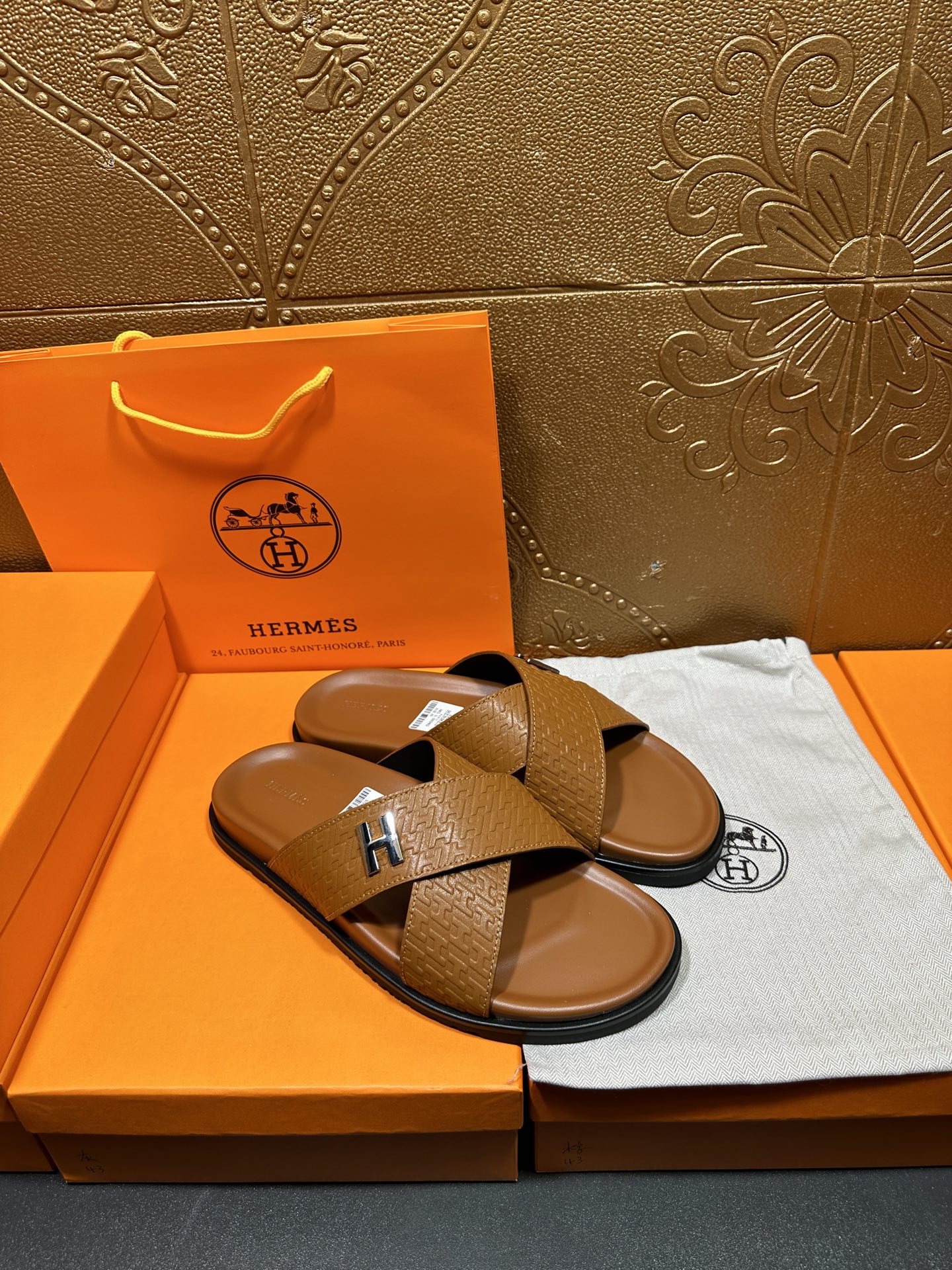 Hermes slide sandals with tan textured cross straps and H buckle, one sandal angled