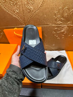 Blue slide sandal with H logo strap and black footbed, back view in hand