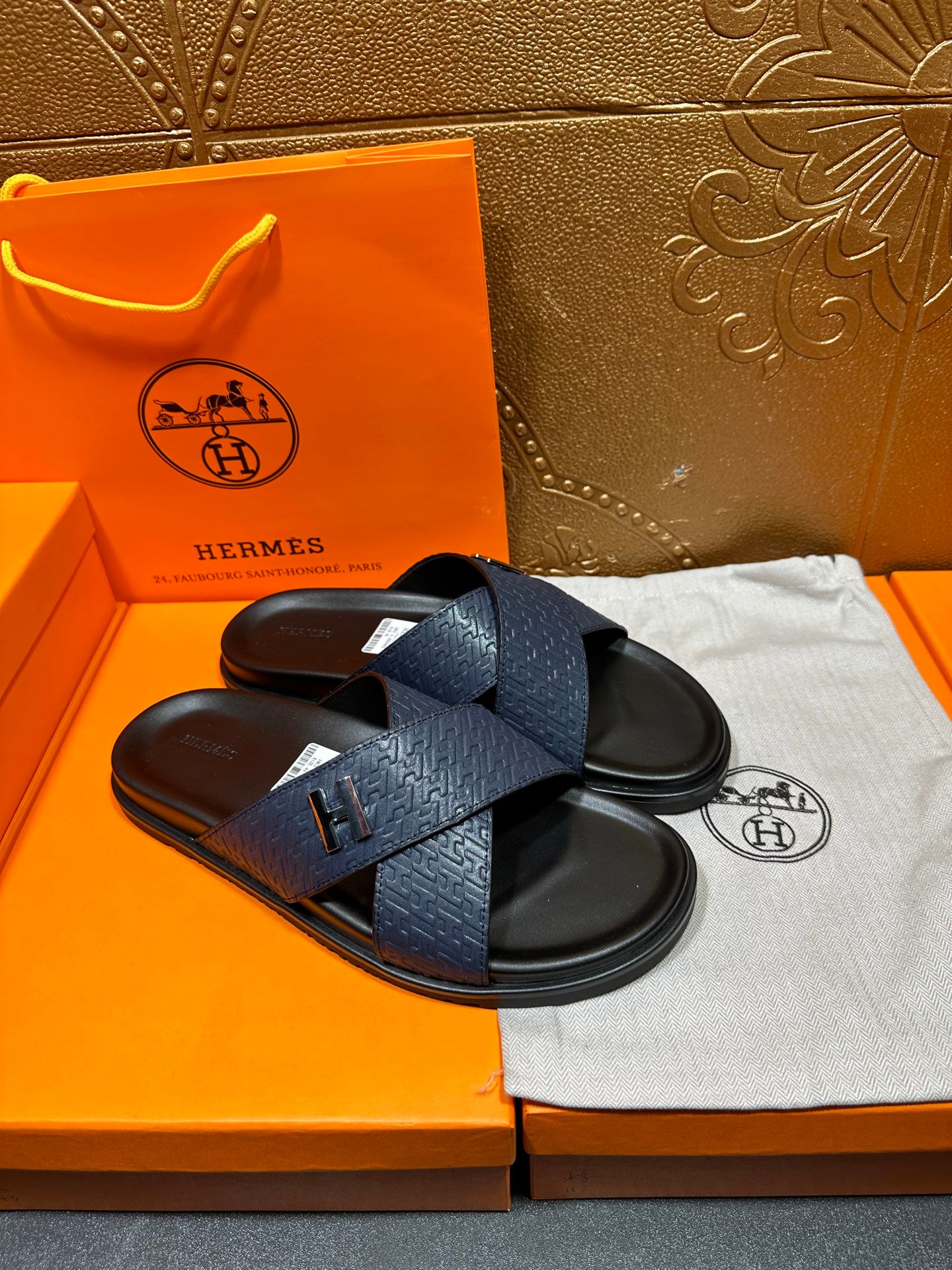 Blue slide sandals with H logo strap detail and black footbed, pair on display