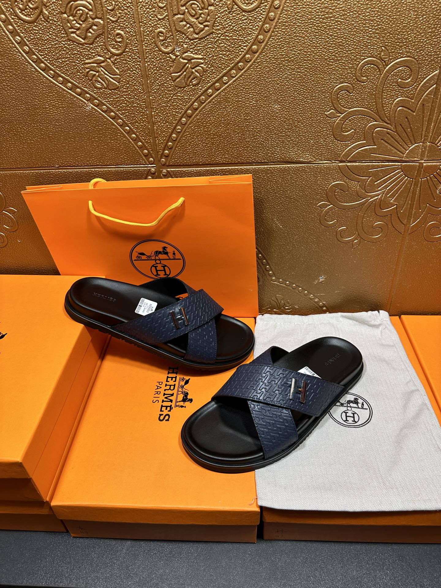 Blue slide sandals with H logo strap and textured pattern, black footbed, pair