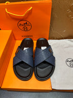 Blue slide sandals with H logo cross straps and black footbed, shown as a pair