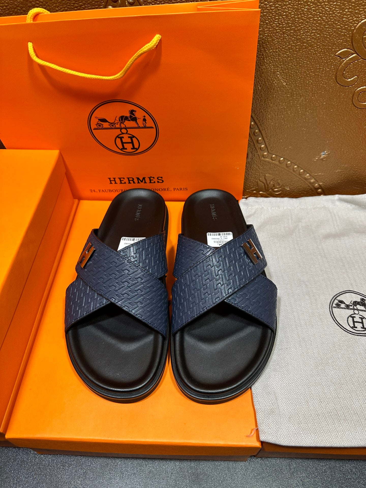 Blue slide sandals with H logo cross straps and black footbed, shown as a pair