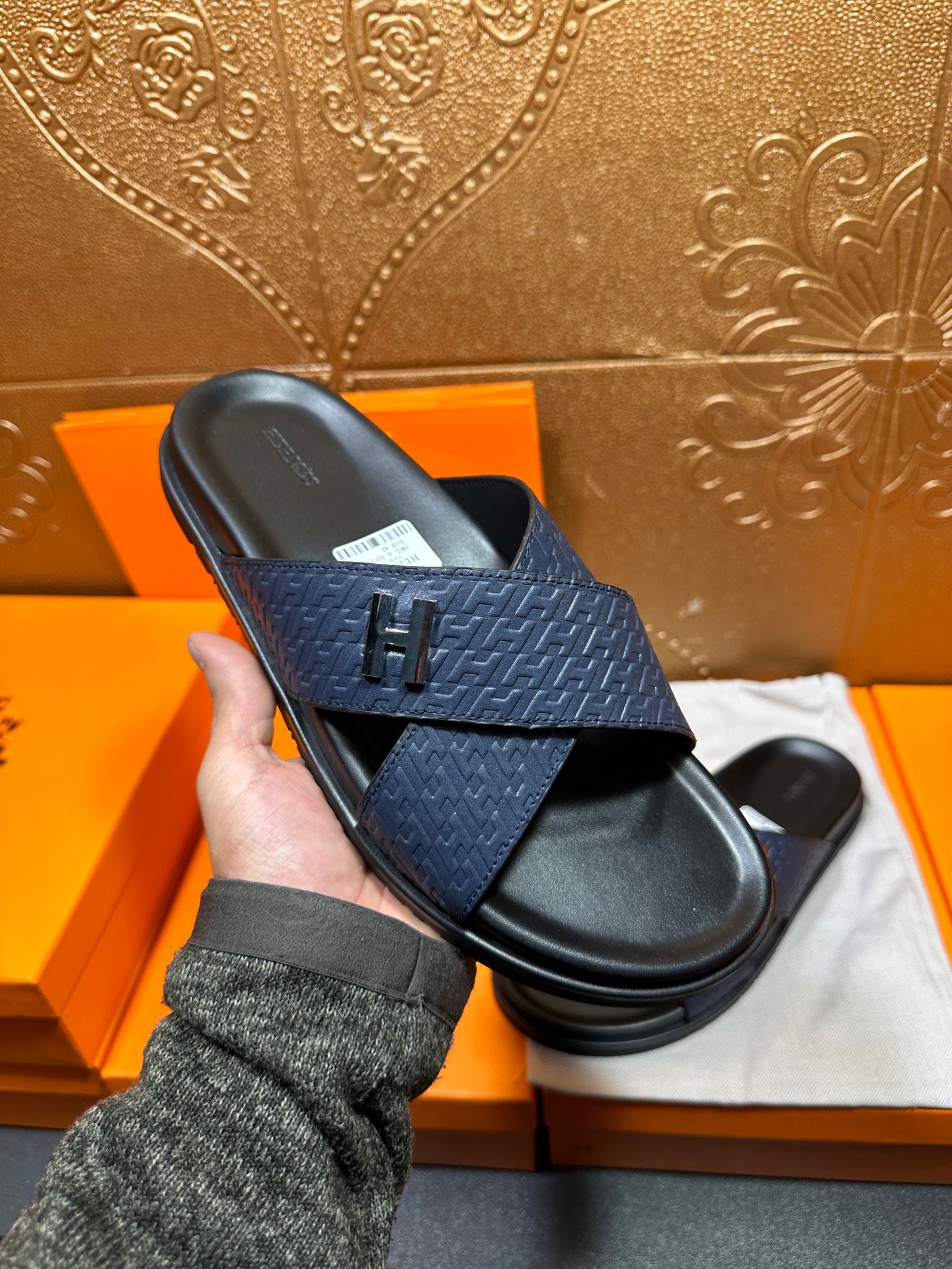 Blue slide sandal with textured strap and H logo detail, black sole shown in hand