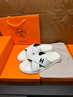 Hermes white slide sandals with textured straps and black H logo on footbed
