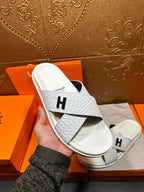 Hermes white leather slide sandals held in hand, black H logo strap