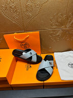 Hermes sandals with light gray straps and black footbed, H buckle, angled view