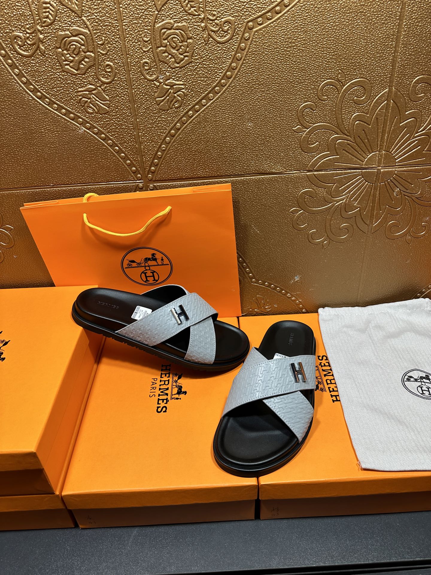 Hermes sandals with light gray straps and black footbed, H buckle, angled view
