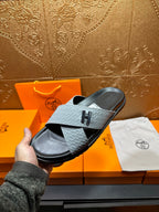 Hermes sandals on hand with light gray textured strap and black footbed, H detail