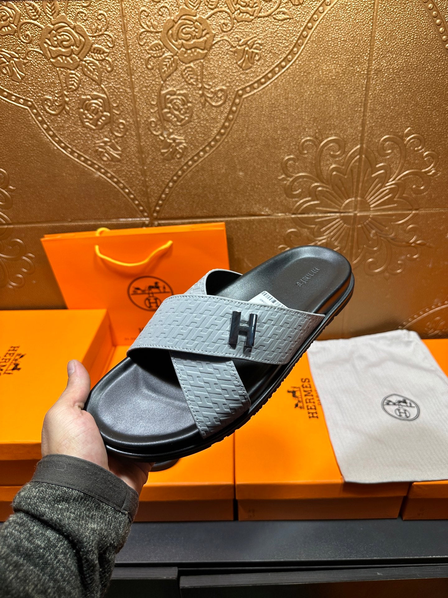Hermes sandals on hand with light gray textured strap and black footbed, H detail