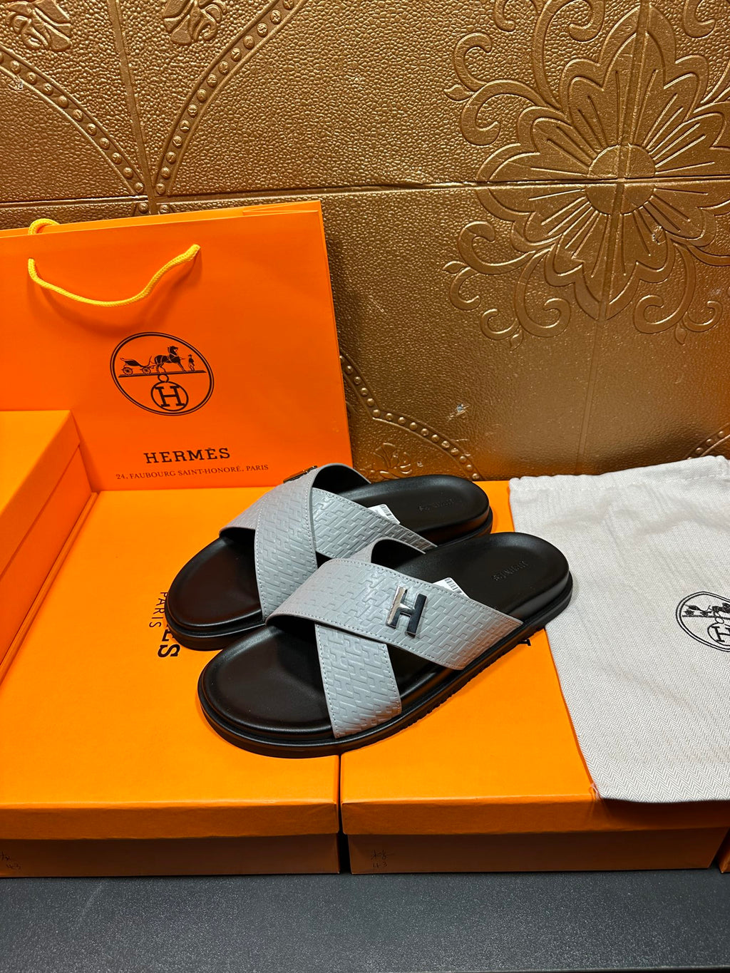 Hermes sandals showing light gray textured strap with H buckle over black base
