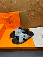 Hermes sandals showing light gray textured strap with H buckle over black base