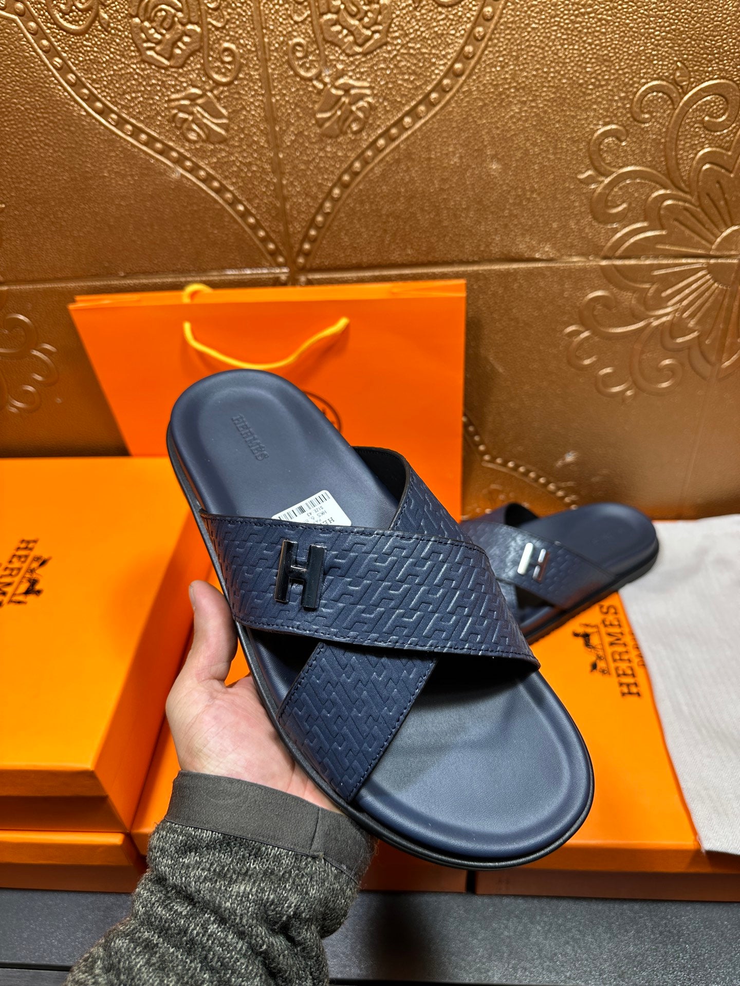 Navy textured slide sandals held in hand, showing H logo buckle