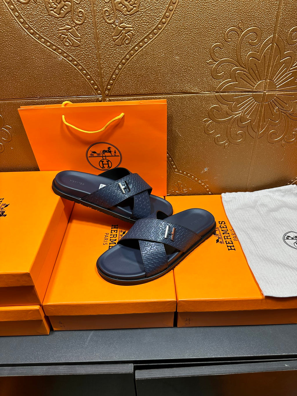 Navy textured slide sandals with H logo buckle, resting on box