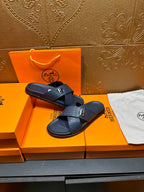 Navy textured slide sandals with H logo buckle, resting on box