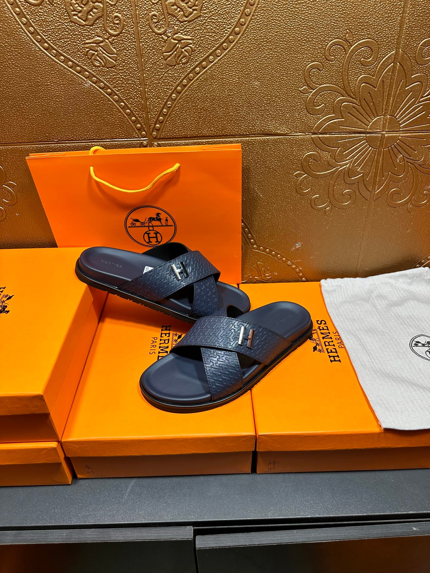 Navy textured slide sandals with H logo buckle, resting on box