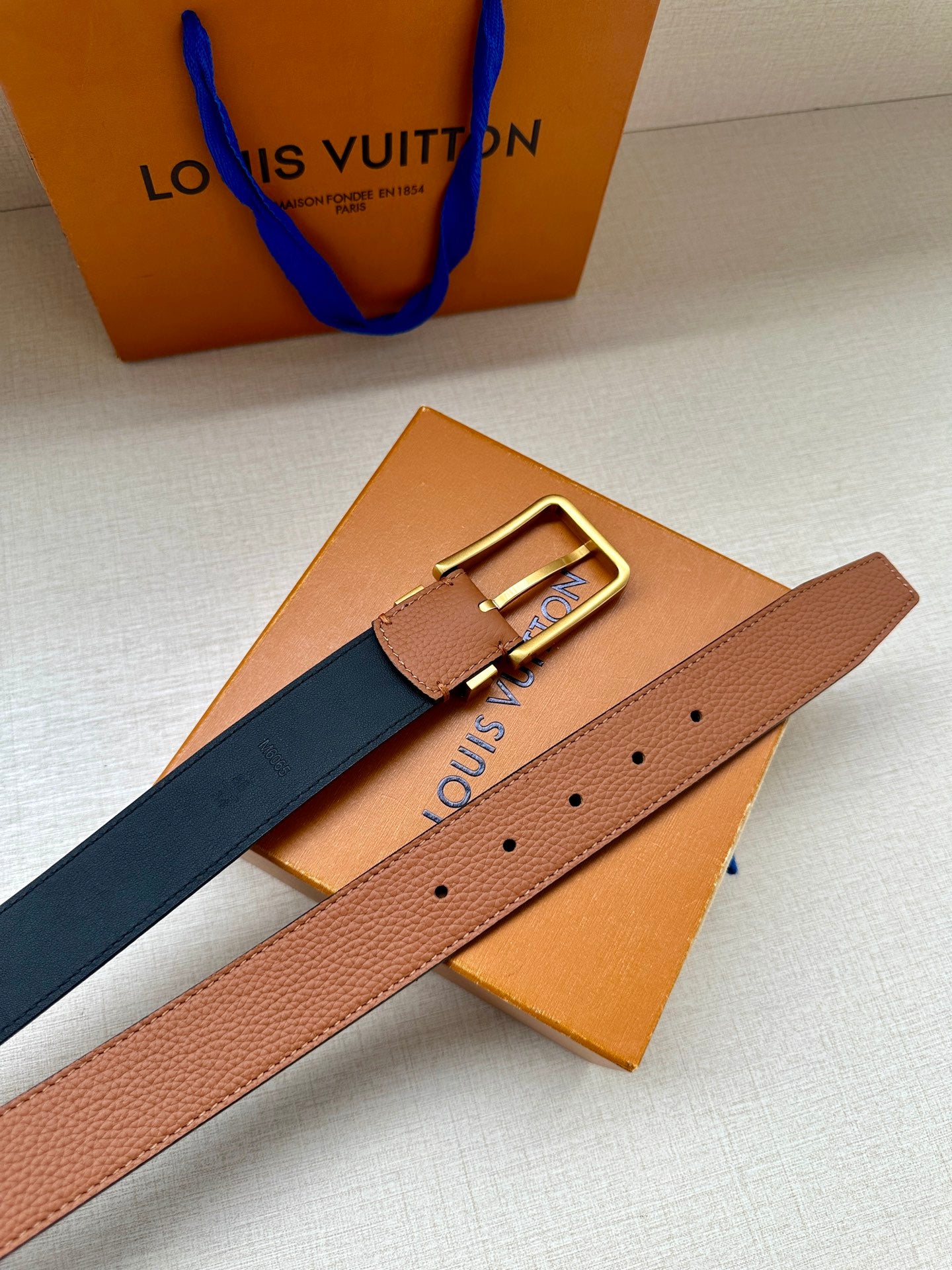 Louis Vuitton leather belt flat lay, tan and dark navy straps with gold buckle