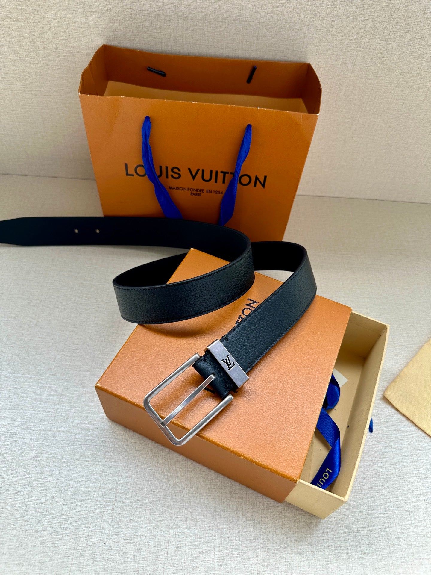 Louis Vuitton belt with dark blue strap and silver-toned buckle in orange box.