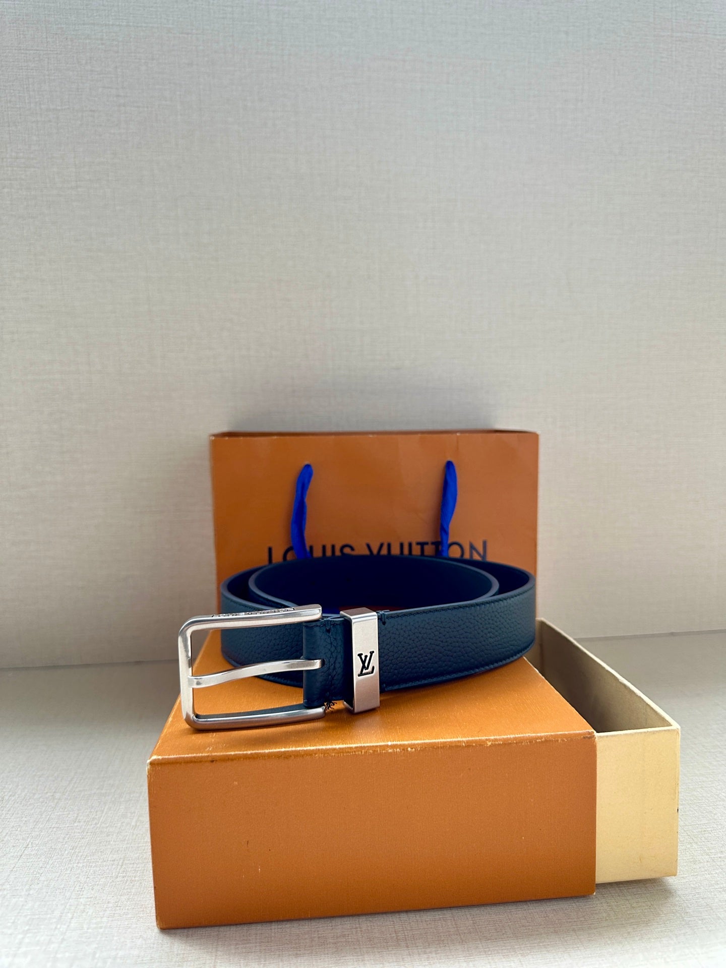 Louis Vuitton belt on box, dark blue leather strap with silver-toned buckle.