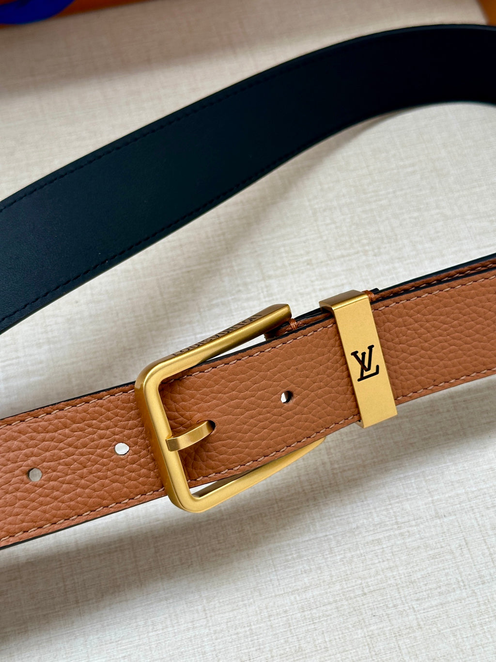 Louis Vuitton leather belt close-up, tan strap with gold buckle and LV plaque