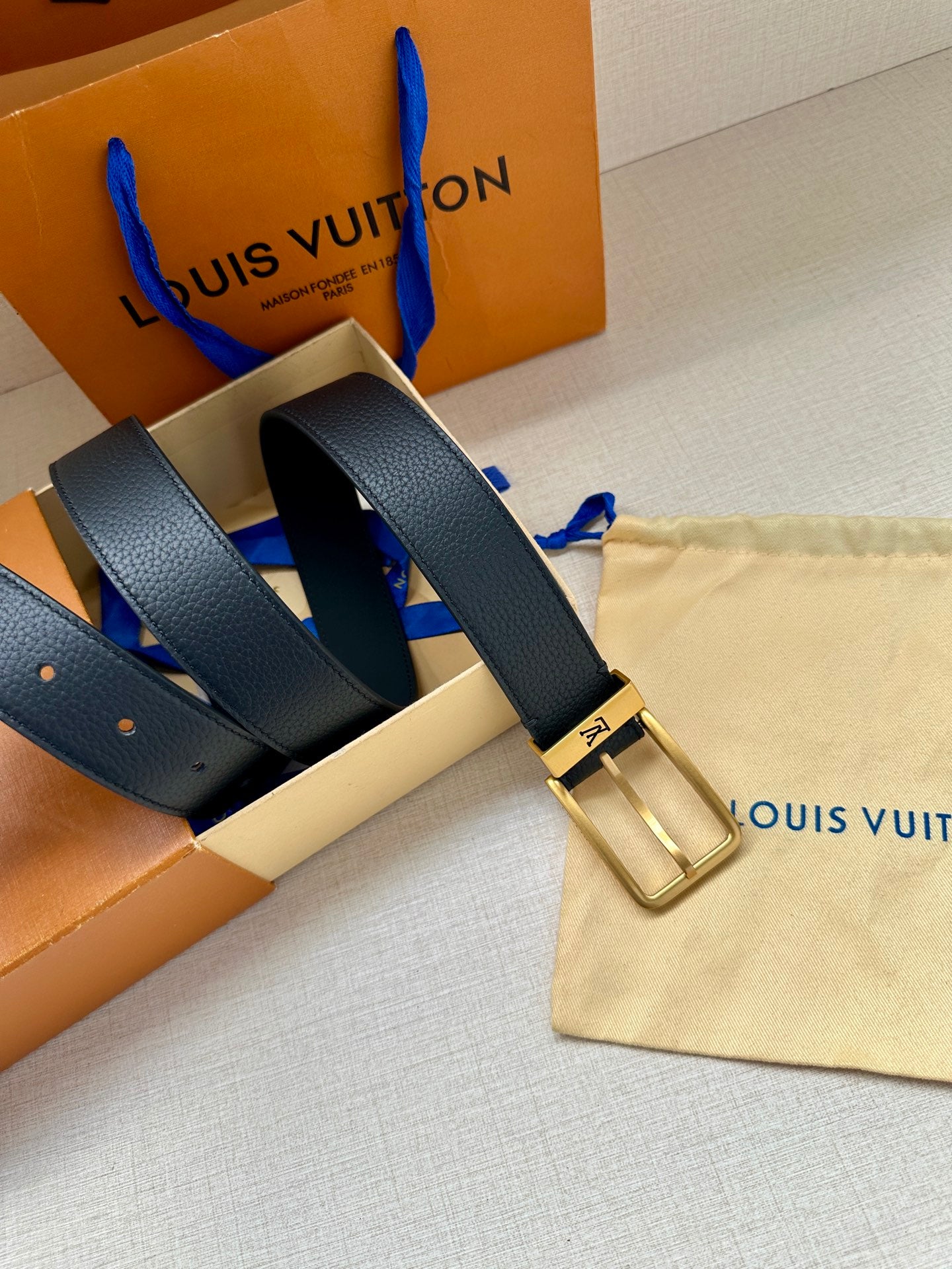 Louis Vuitton belt laid out flat, dark blue strap with gold-tone buckle.