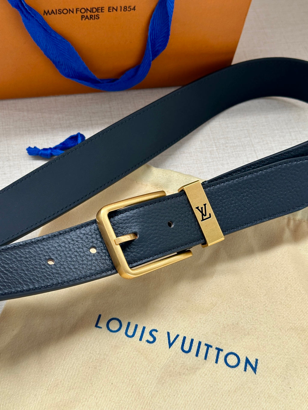 Louis Vuitton belt detail, dark blue leather strap with gold-tone square buckle.