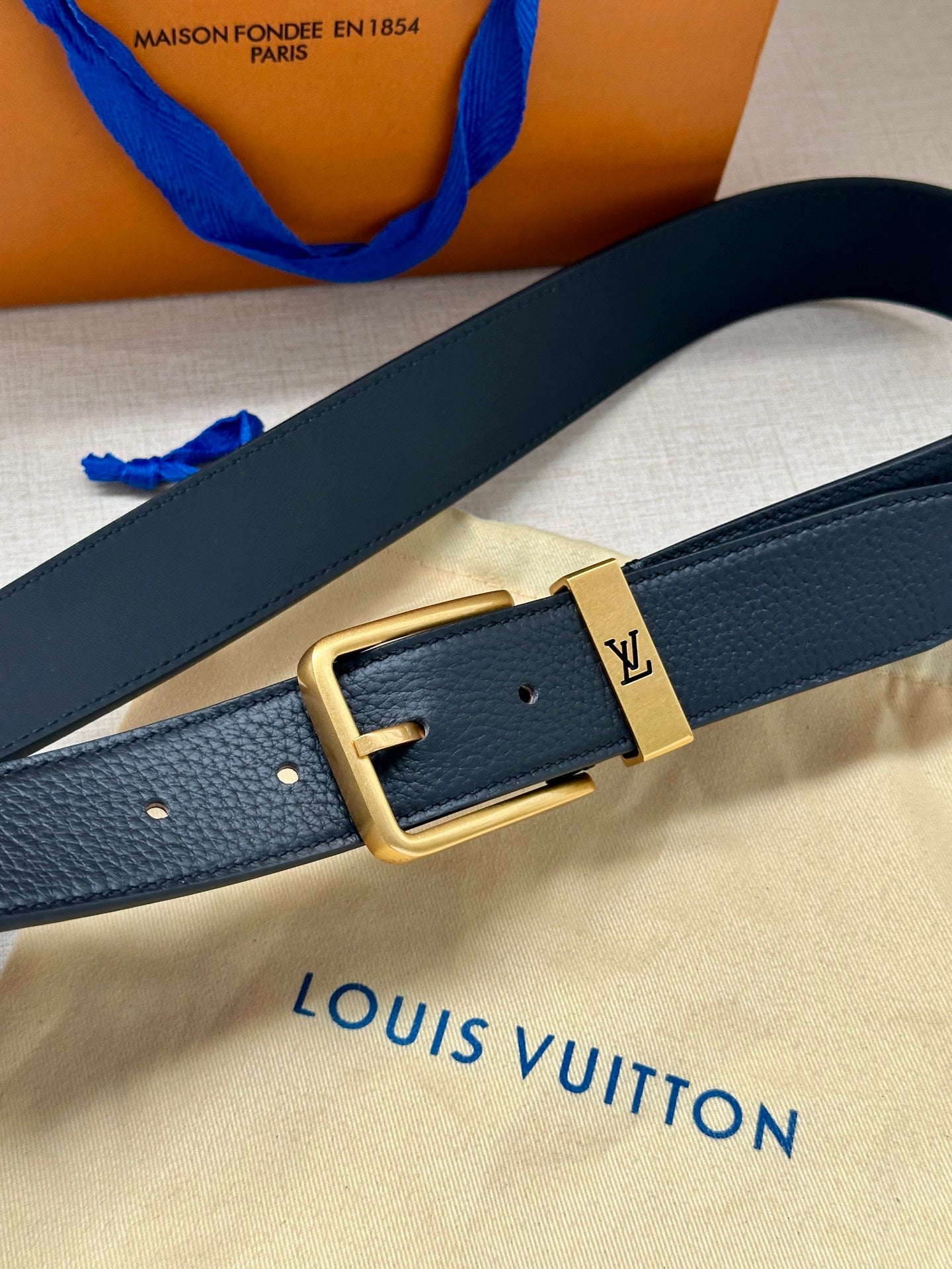 Louis Vuitton belt detail, dark blue leather strap with gold-tone square buckle.