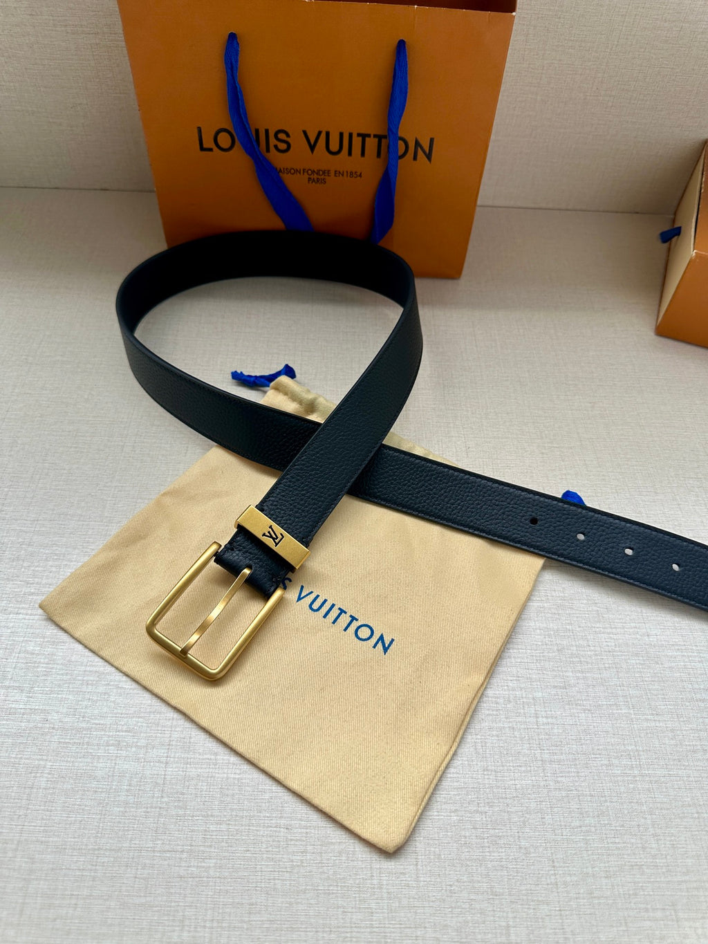 Louis Vuitton belt with dark blue leather strap and gold-tone buckle on dust bag.