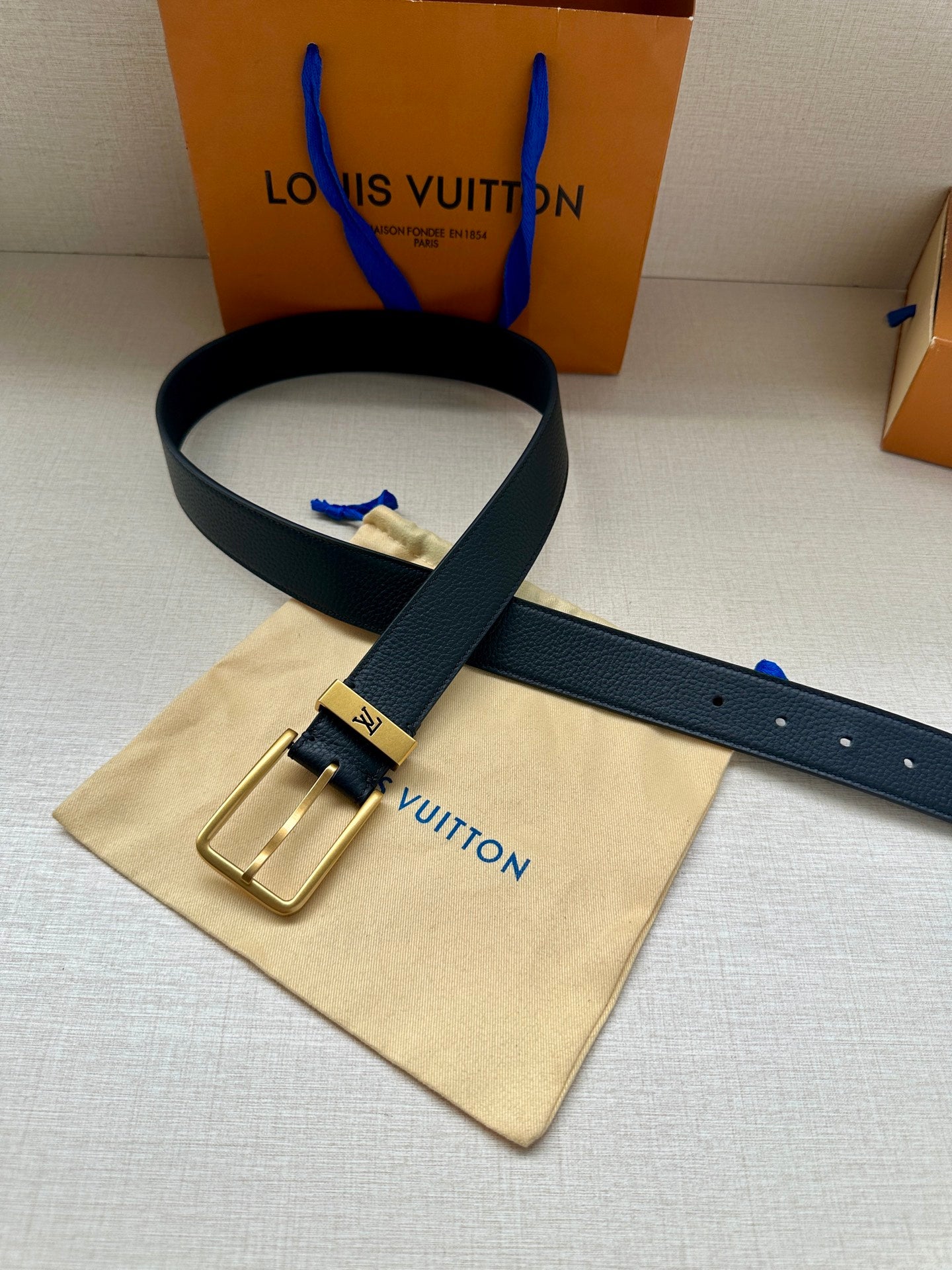 Louis Vuitton belt with dark blue leather strap and gold-tone buckle on dust bag.