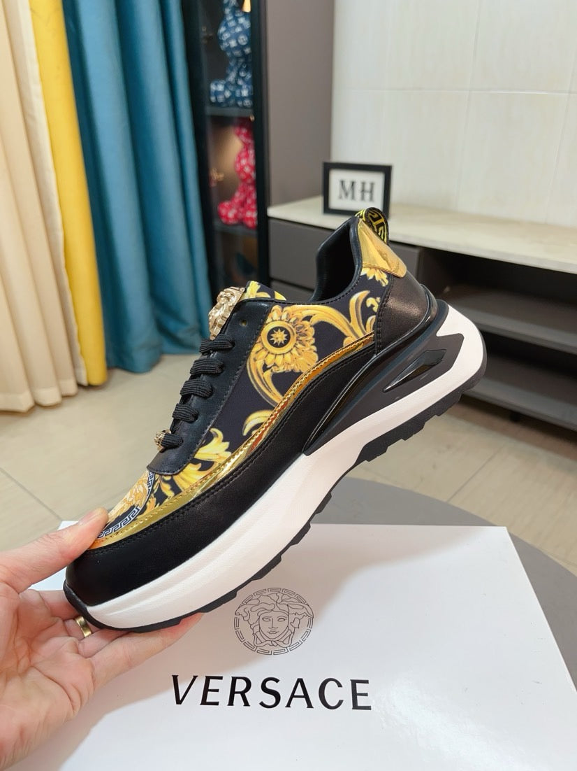 Black lace-up sneakers with gold baroque panel and emblem at the tongue, thick white sole.