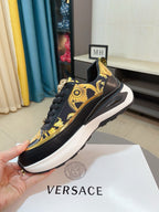 Black lace-up sneakers with gold baroque panel and emblem at the tongue, thick white sole.