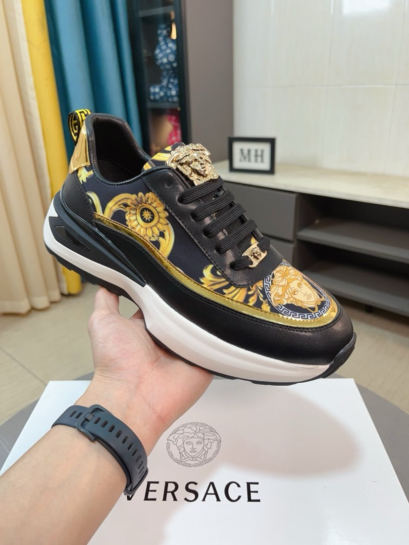 Black and gold designer sneakers, lace-up style with ornate medallion detail, thick sole.