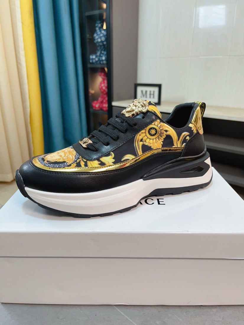 Black lace-up sneakers with gold baroque print and Medusa-style emblem, chunky white sole.
