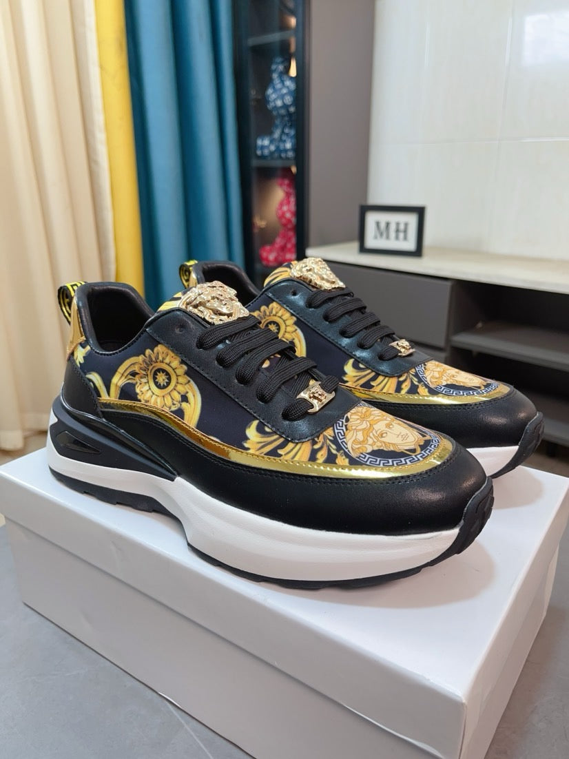 Pair of black lace-up sneakers with gold baroque graphics, Medusa-style emblem, white sole.