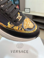 Close-up of black lace-up sneaker upper with gold baroque panel and ornate medallion detail.