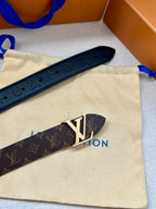 Monogram belt with dark strap and gold-tone LV buckle on a beige pouch