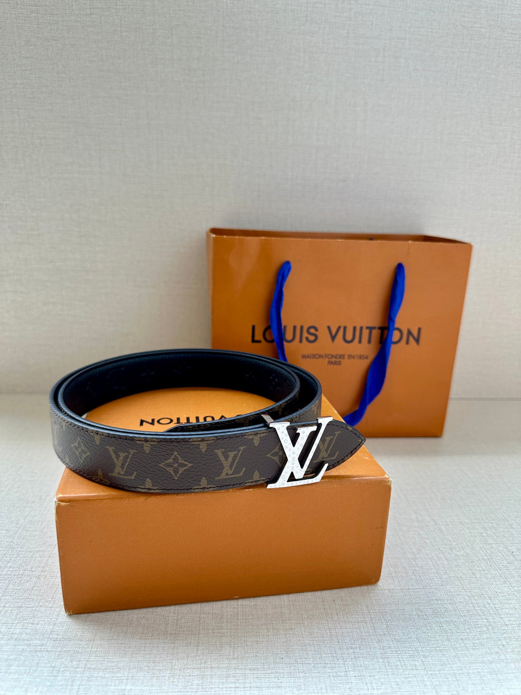 Monogram belt with dark strap and gold-tone LV buckle resting on box